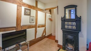A room with exposed wooden beams, a fireplace with a decorative mantle, a flat-screen TV on a glass stand, and framed pictures on the wall. - 3 bedroom accommodation in Ludlow (Ludlow)