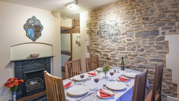 A dining room with a stone wall, a fireplace, and a table set for four. - 3 bedroom accommodation in Ludlow (Ludlow)
