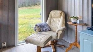 A room with a large window, a leather chair with a footrest, a small wooden table with a plant, and a cabinet. - 3 bedroom nice home in Mjosundet (Mjosundet)