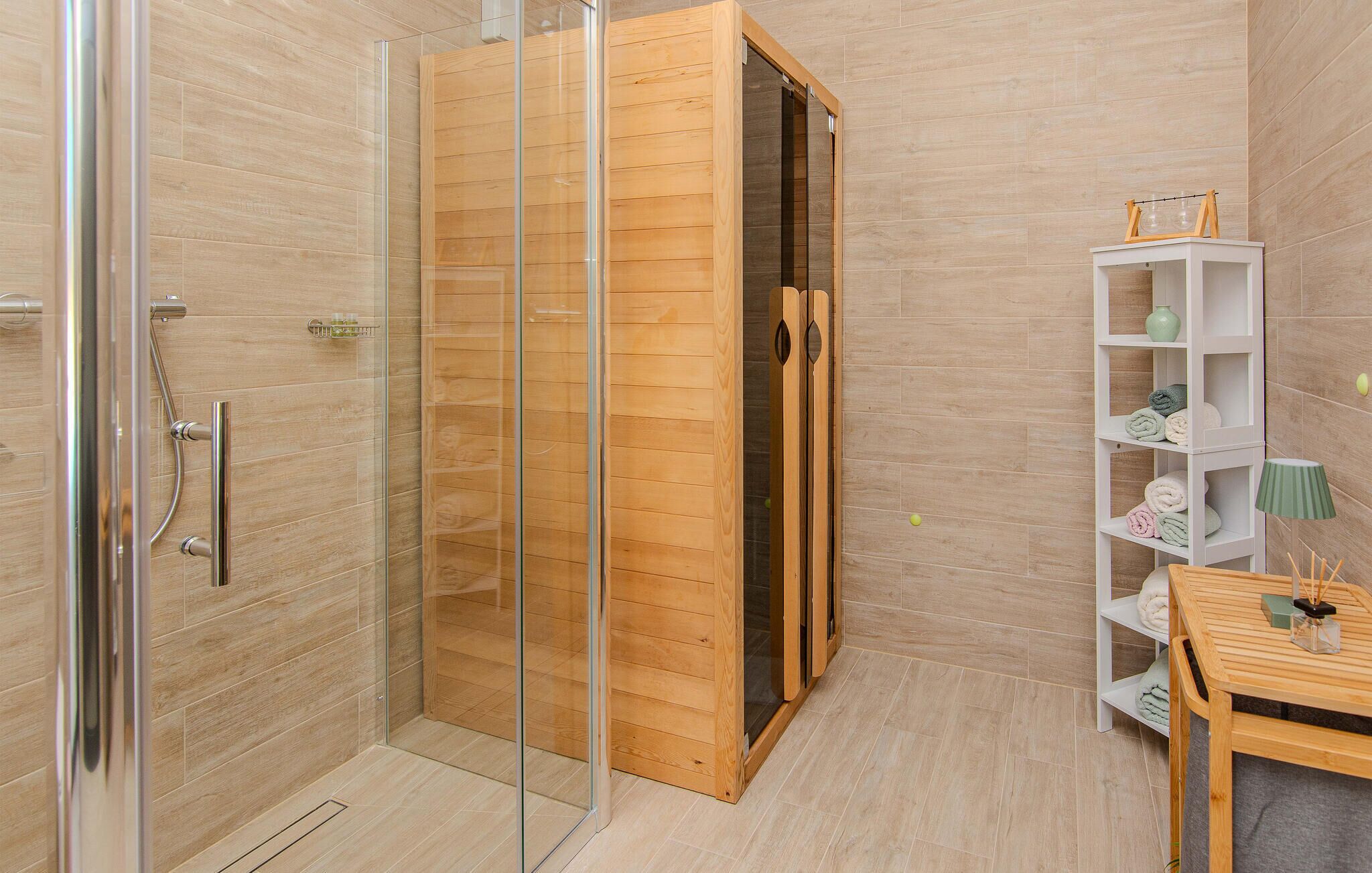 A modern bathroom with a glass shower enclosure, wooden door, and a white shelf with towels.