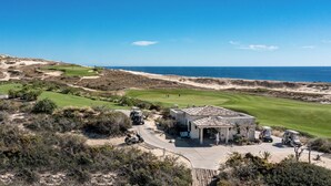 Un parcours de golf situé sur la côte, avec un club-house, des dunes de sable et l’océan en toile de fond.