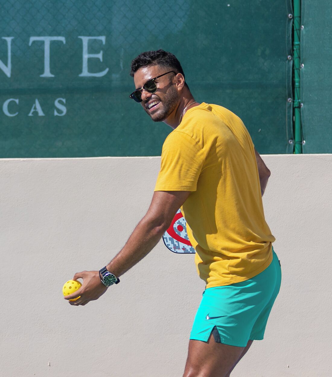 Un hombre con una camisa amarilla y pantalones cortos turquesa jugando tenis.