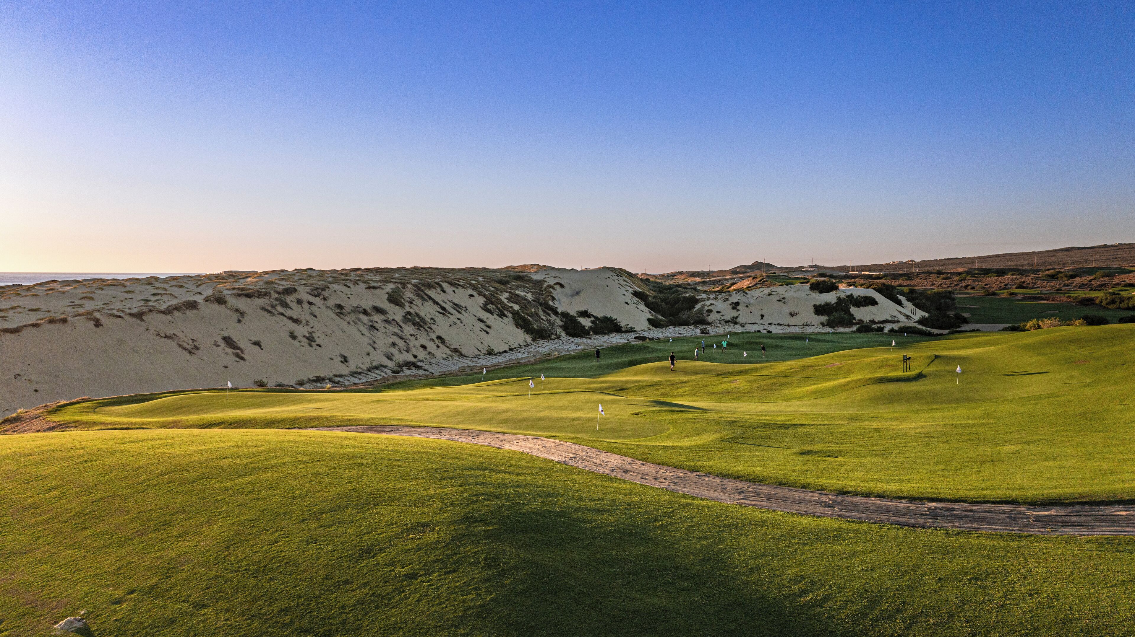 A golf course with a clear path, sand dunes, and a flag on the green.