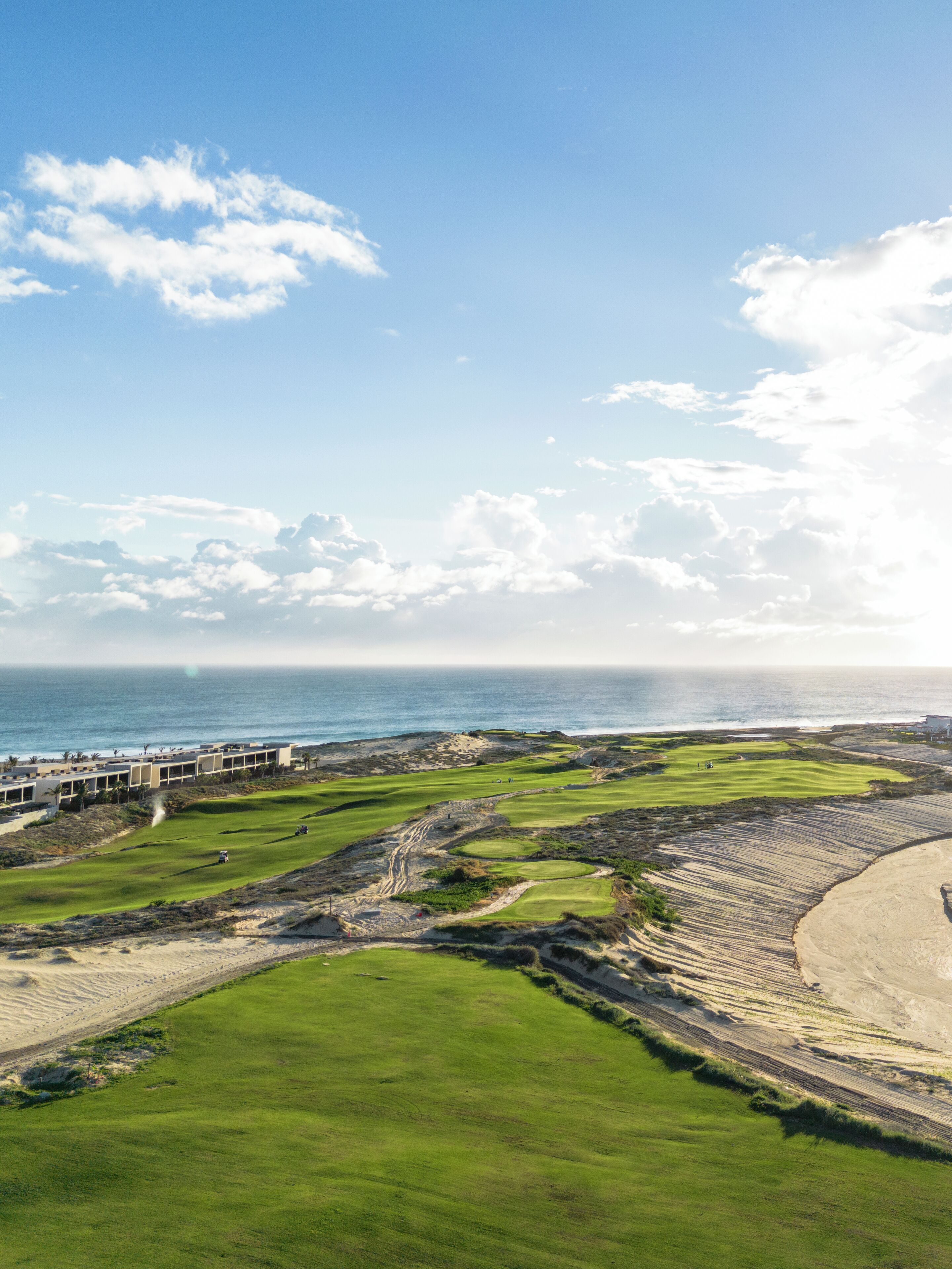 A golf course with a view of the ocean and a building in the background.