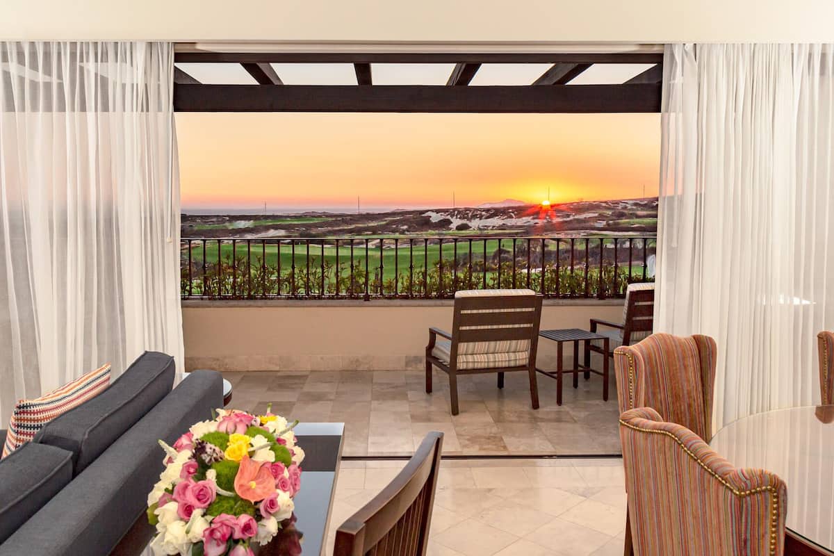 Varanda com vista para um pôr do sol sobre um campo de golfe, mobiliada com sofá, cadeiras e uma mesa.