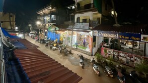 Une vue de rue nocturne avec un restaurant Prasad proposant des repas sur place, des motos garées et des immeubles dotés de balcons.