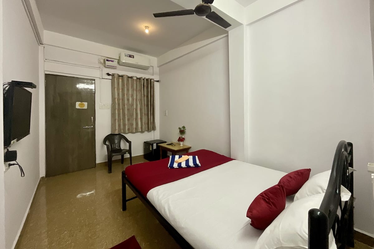 A hotel room with a bed, a desk, a chair, an air conditioning unit, and a ceiling fan.