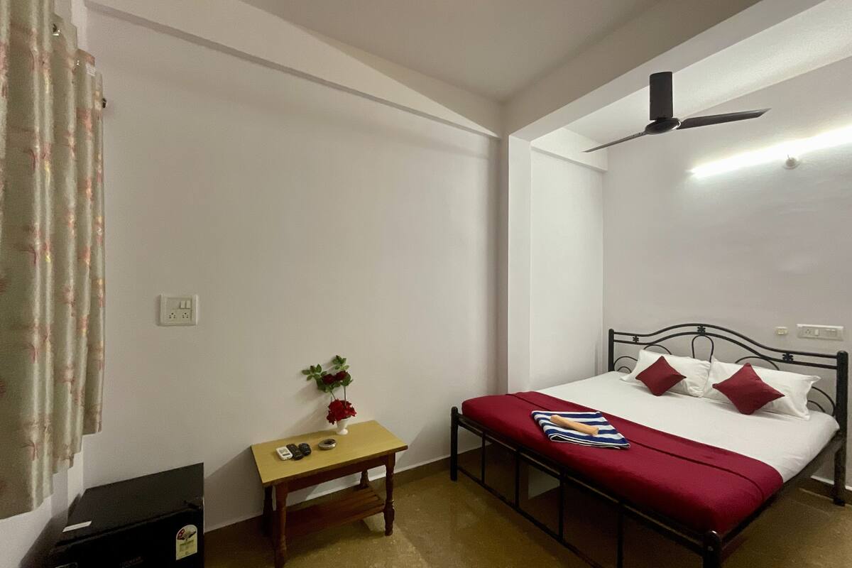 A bedroom with a single bed, a bedside table with a vase of flowers, a ceiling fan, and a small table with a telephone and a remote control.