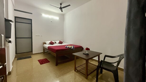 Une petite pièce bien éclairée, avec un lit, une table, une chaise et un ventilateur de plafond.