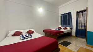 Une chambre avec deux lits, chacun étant équipé de draps et d’oreillers rouges, une petite table et une fenêtre avec des rideaux.