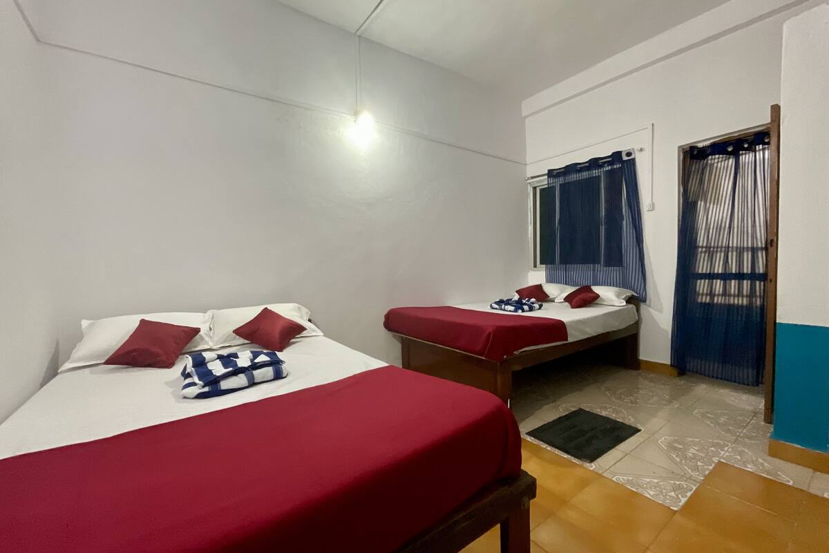 A room with two beds, each with red bedding and pillows, a small table, and a window with curtains.