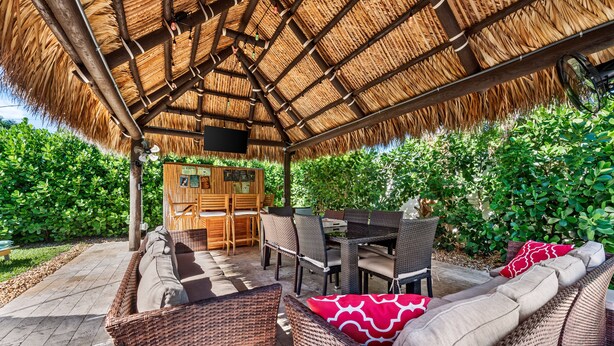 Una terrazza esterna con mobili in vimini, un tetto di paglia e un tavolo in legno.