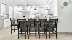 Una cucina moderna con mobili bianchi, un'isola centrale con posti a sedere, luci a sospensione e un trave in legno rustico.