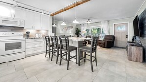 Una cucina moderna con mobili bianchi, un'isola centrale con sedute e un ventilatore a soffitto, oltre a una grande finestra.