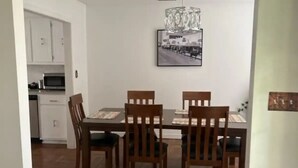 Et spiseområde med et træbord og stole, en lysekrone og et køkken i baggrunden.