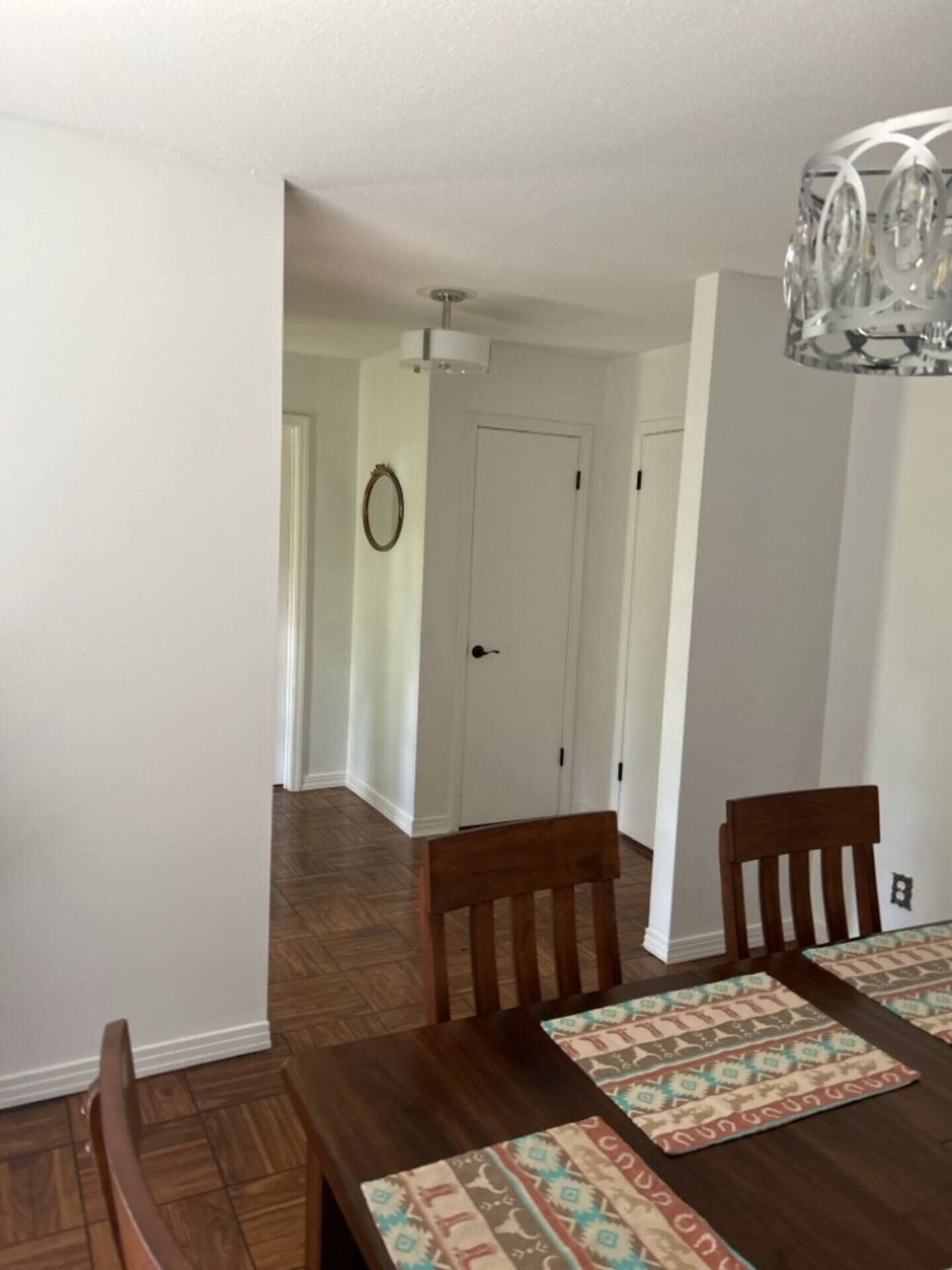 A dining area with a wooden table and chairs, patterned placemats, and a hanging light fixture.