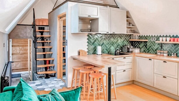 A compact kitchen with a herringbone tile backsplash, wooden bar stools, and a small island.