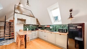A compact kitchen with a herringbone tile backsplash, a black refrigerator, wooden stools, and a window providing natural light.