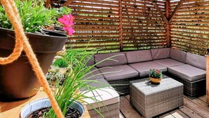 A wooden deck with a gray cushioned seating area, a small table, and potted plants.