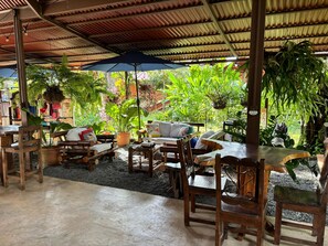 An outdoor seating area with wooden furniture, a covered roof, and lush greenery. - Hacienda Río Oro (Puerto Jiménez)