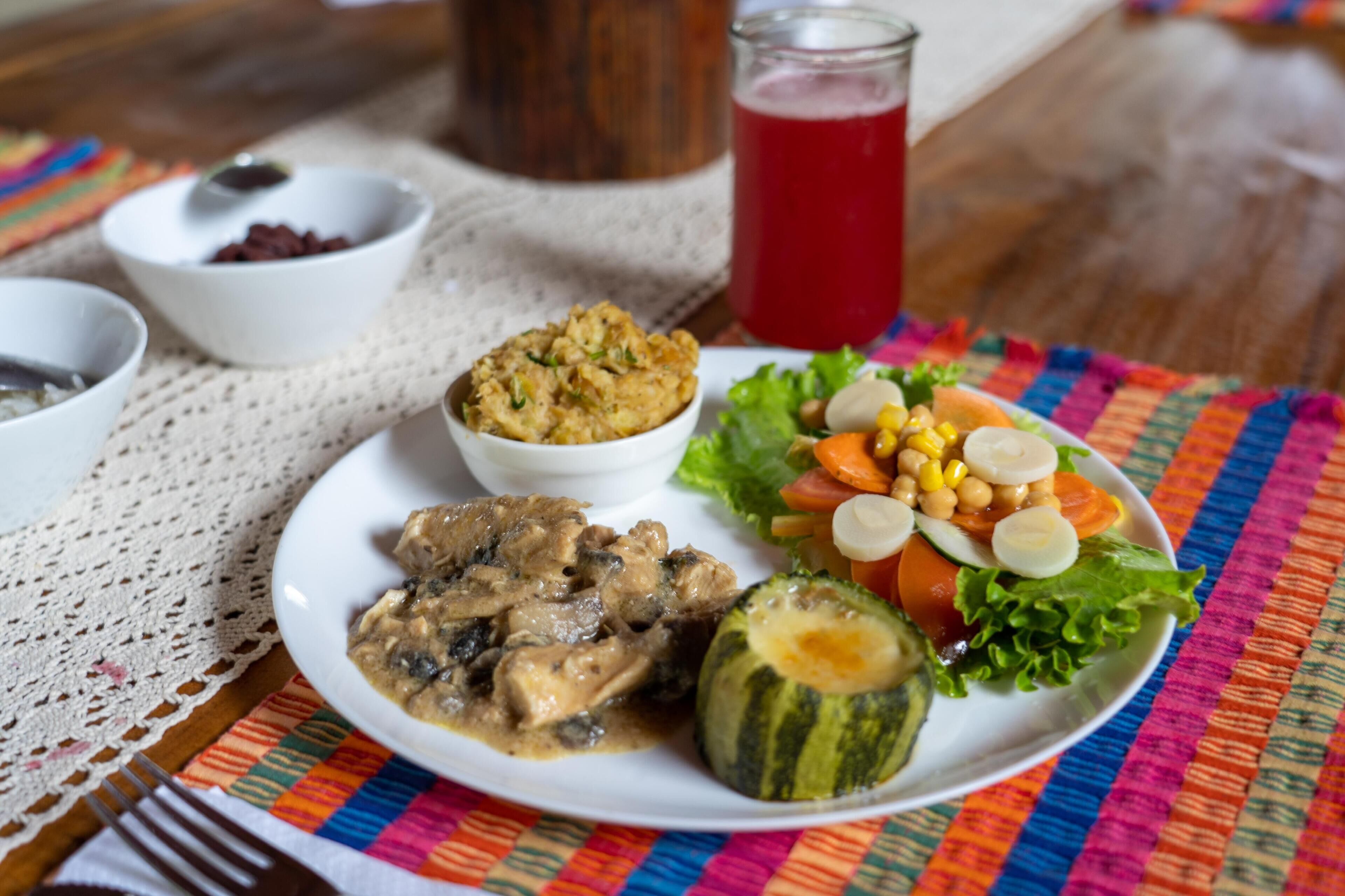 A plate with a salad, a bowl of soup, and a glass of red drink on a table with a colorful tablecloth.