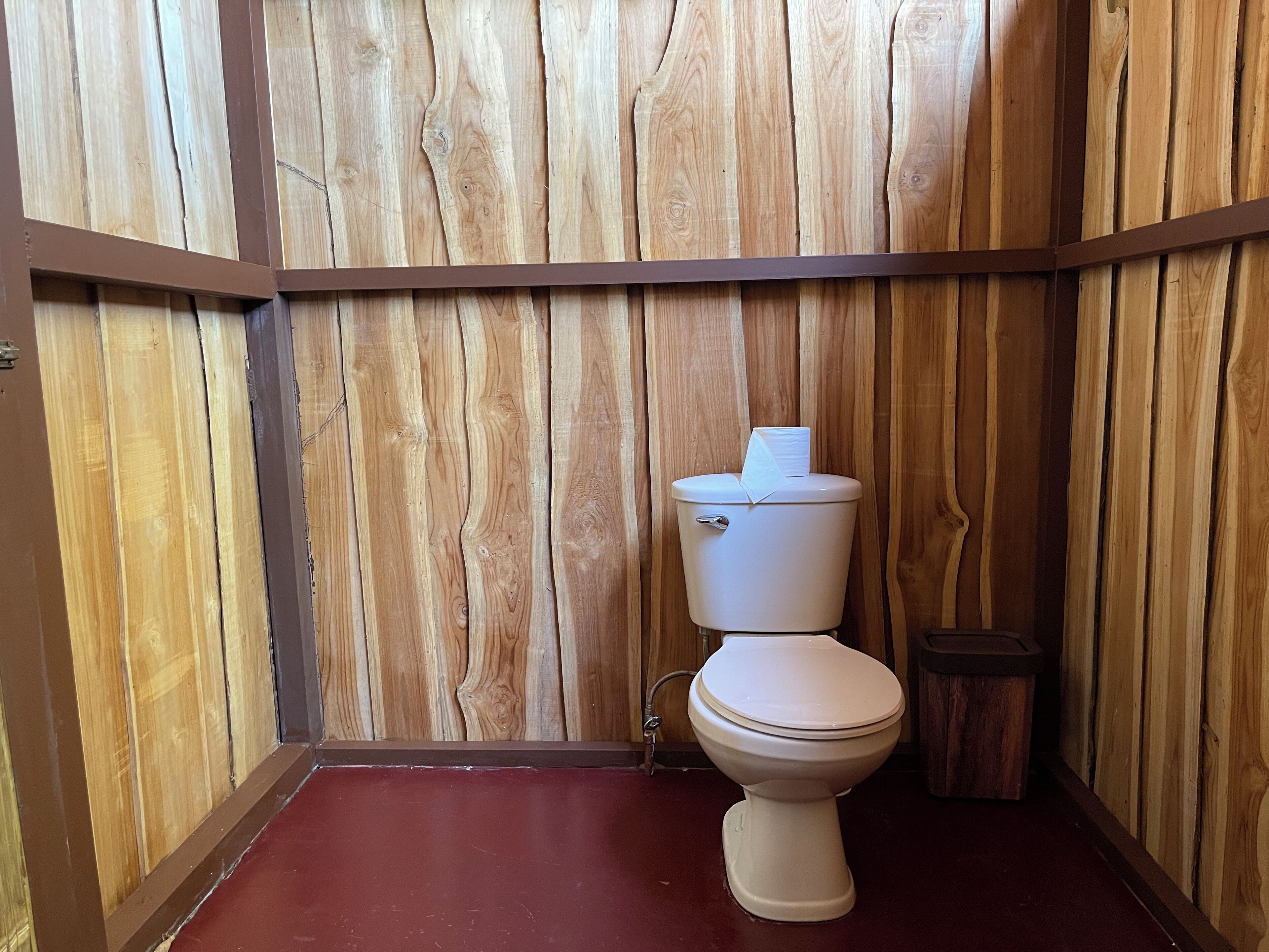 A wooden-paneled bathroom with a white toilet and a trash bin.