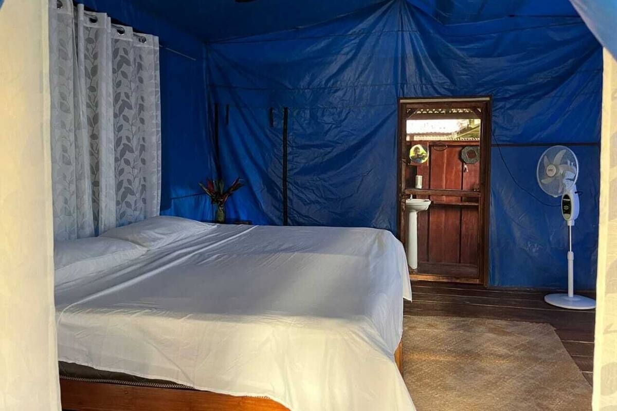 A tented room with a bed, a sink, and a fan.