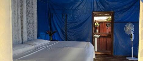 A tented room with a bed, a sink, and a fan.