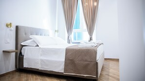 A neatly made bed with a white and brown bedspread, a bedside table with a lamp, and a window with curtains. - Dimora Diaz B&B (Naples)