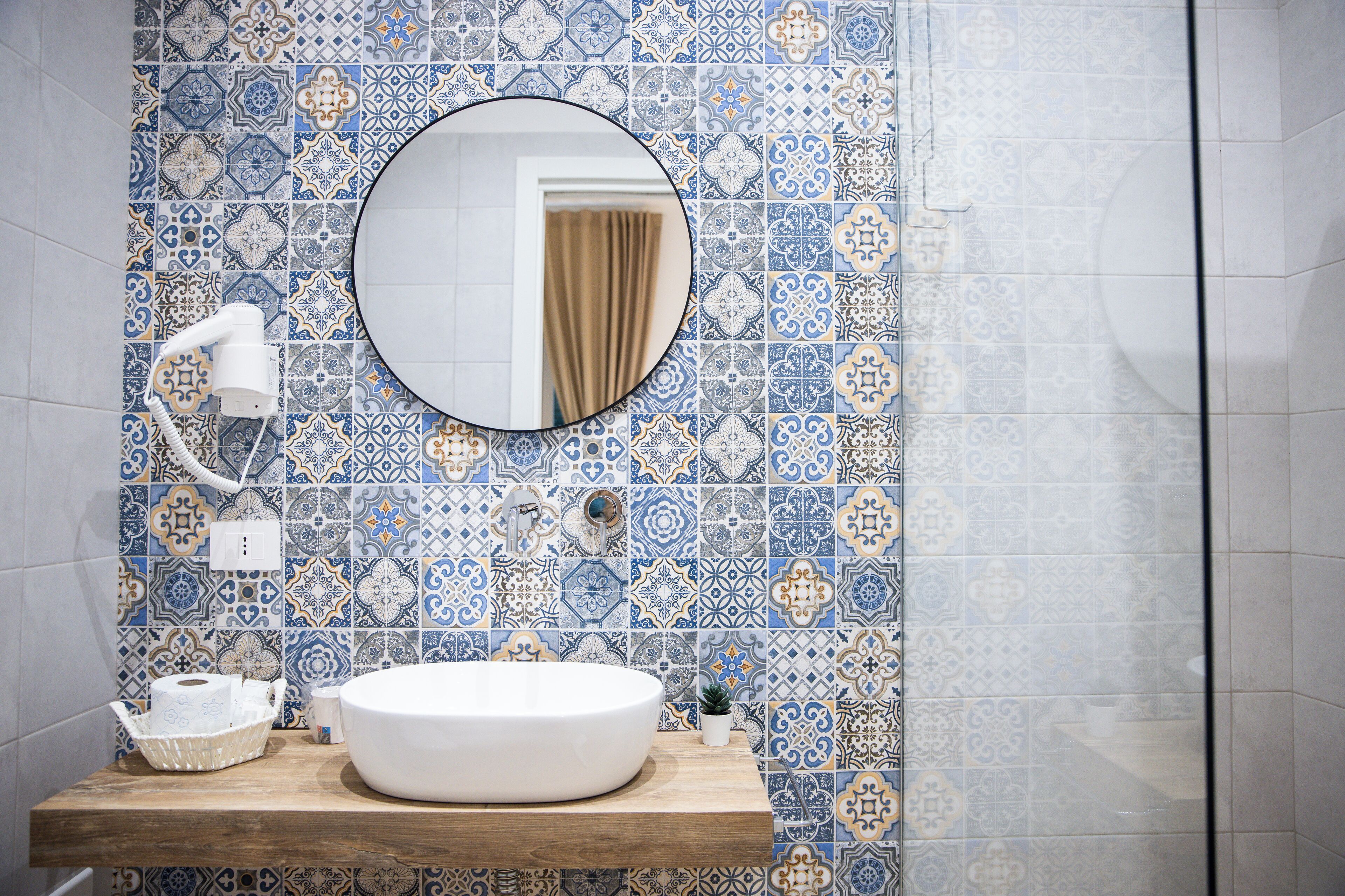 A bathroom with a round mirror, a white sink, and patterned tiles.