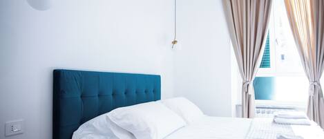 Habitación de hotel con cama, mesita de noche, ventana con cortinas y toma de corriente.