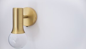 A wall-mounted light fixture with a clear glass bulb and a brass base. - Dimora Diaz B&B (Naples)