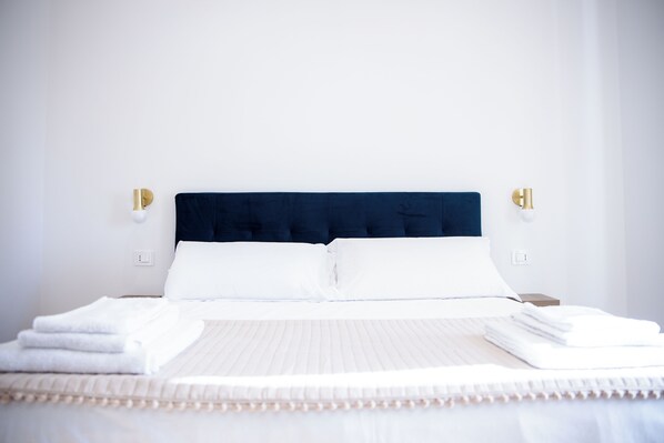 A neatly made bed with white linens and a dark headboard, two bedside lamps, and a clean, minimalist room design.