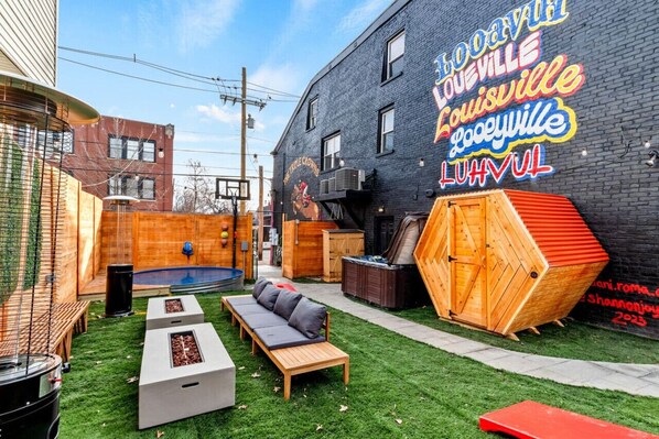 A backyard with a basketball hoop, a wooden bench, a small pool, and a neon sign on the wall.