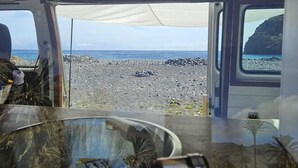 A vehicle interior with a view of a rocky beach and the ocean. - Furgot3 1980 (Agulo)