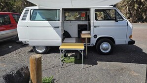 A white van with an open rear door, a small foldable table, and a canopy. - Furgot3 1980 (Agulo)