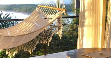 A hammock on a balcony overlooking a river and greenery.
