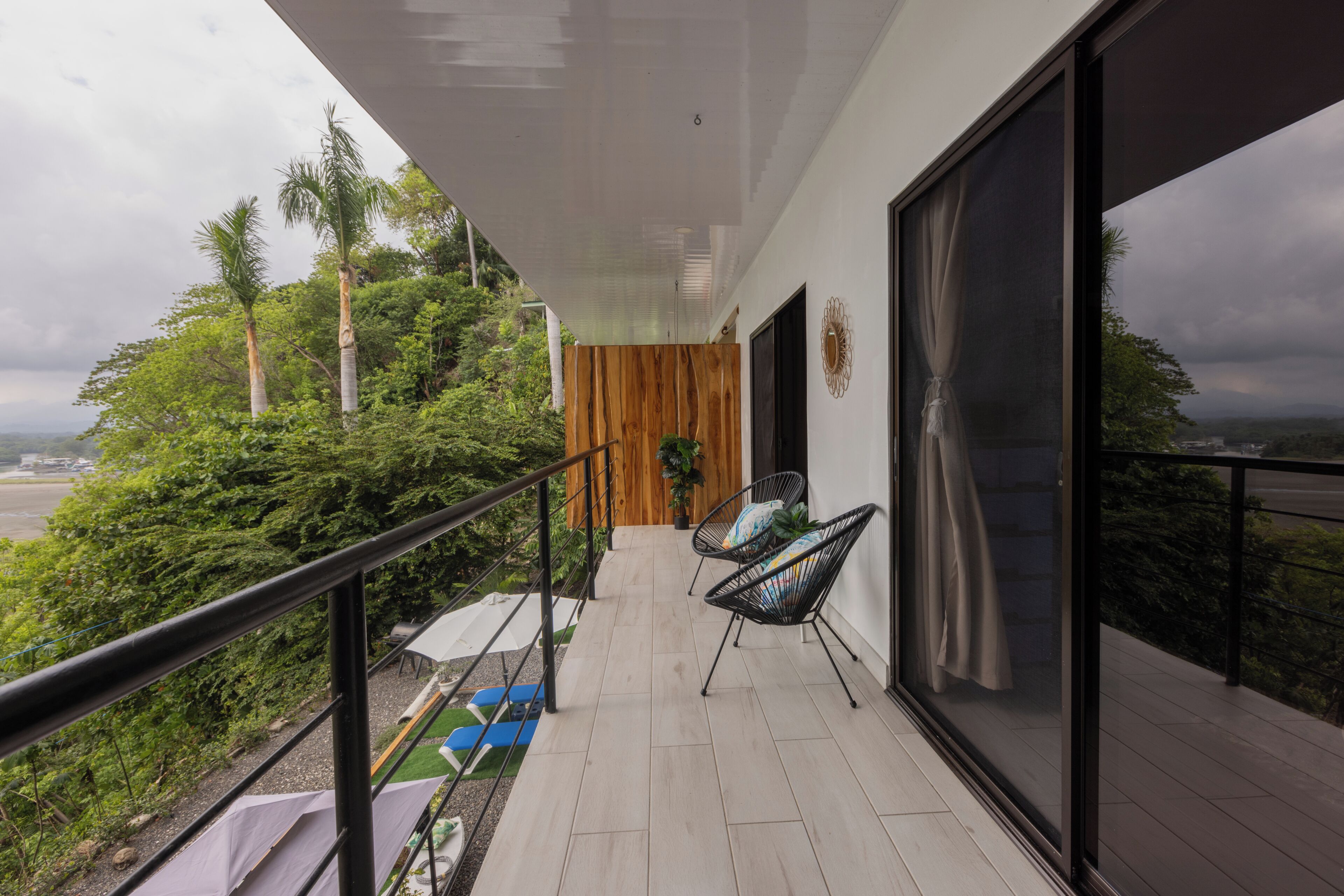 A balcony with a view of the landscape, a wooden wall, and two chairs.