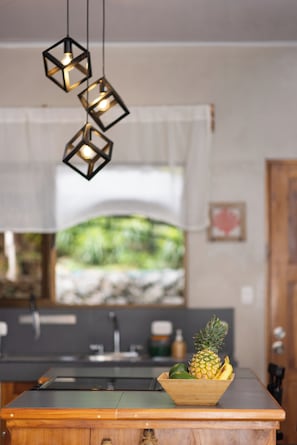 A kitchen with a wooden countertop, a bowl of fruit, and hanging pendant lights. - Mar & Sombra Villas (Quepos)