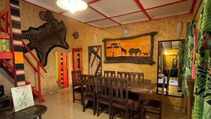 Een eetruimte met een grote tafel en stoelen, een trap met rode leuningen en een muur met een schilderij van dieren.