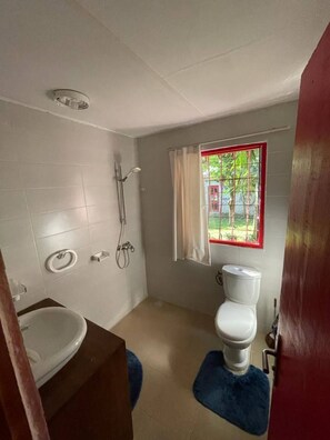 Un baño pequeño con inodoro, ducha y lavamanos. Se ve un ventanal con vistas a la vegetación.