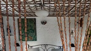 Een bed met een metalen frame en een beddegoed met een patroon, een muur met een schilderij, en een plafond met een geweven ontwerp.