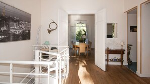 Un couloir avec un escalier, un coin repas avec une table et des chaises, et une vue sur l’extérieur par une porte ouverte.