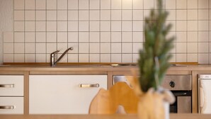 Keittiössä on laatoitettu välitila, ruostumattomasta teräksestä valmistettu pesuallas, puukaapit ja valkoinen jääkaappi.