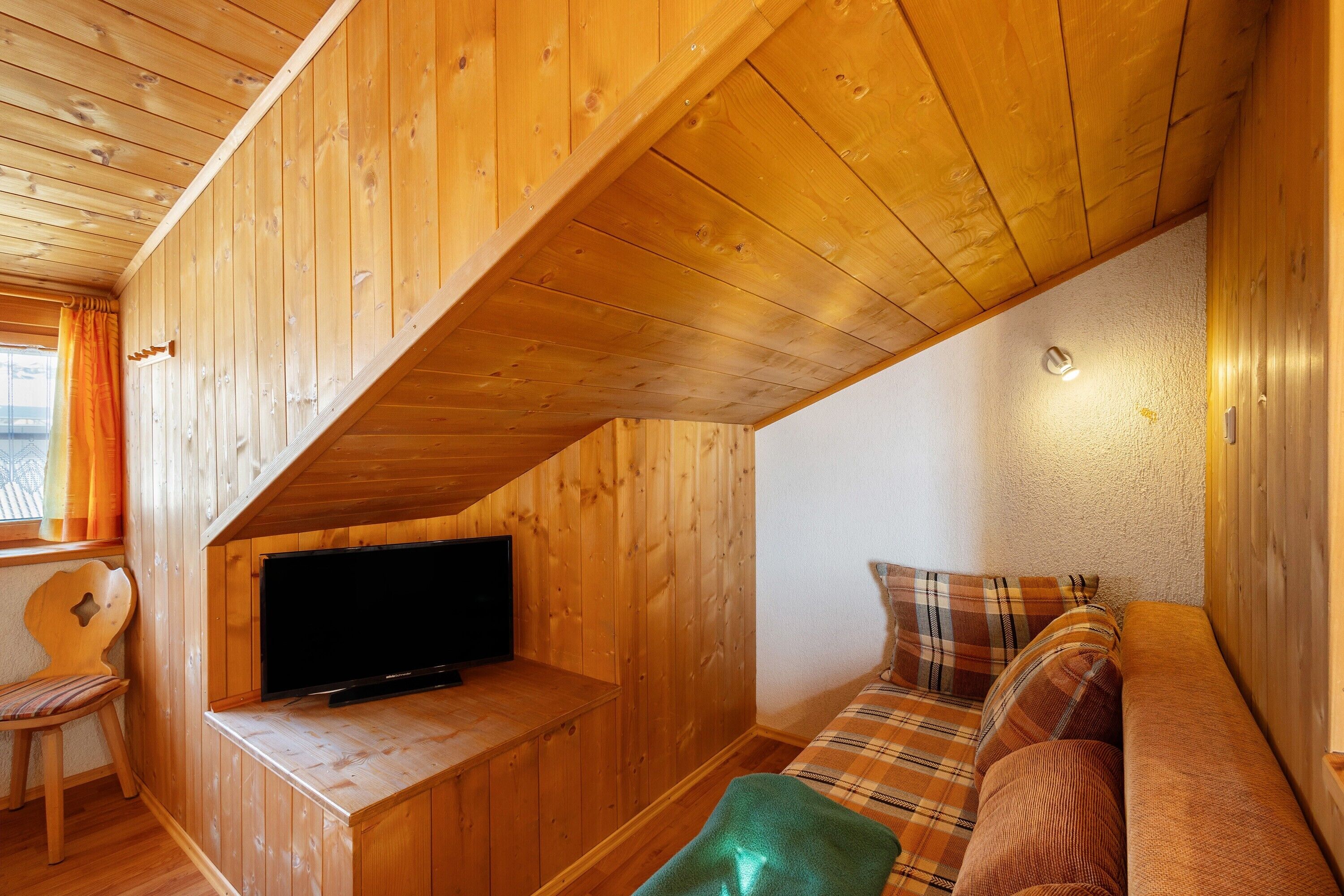 A wooden interior with a television on a low shelf, a plaid sofa, and a wooden chair.