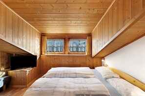 A wooden cabin room with a bed, a television, and a window with curtains.