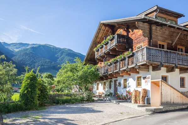 A wooden chalet with balconies, a gravel driveway, and a mountain backdrop.