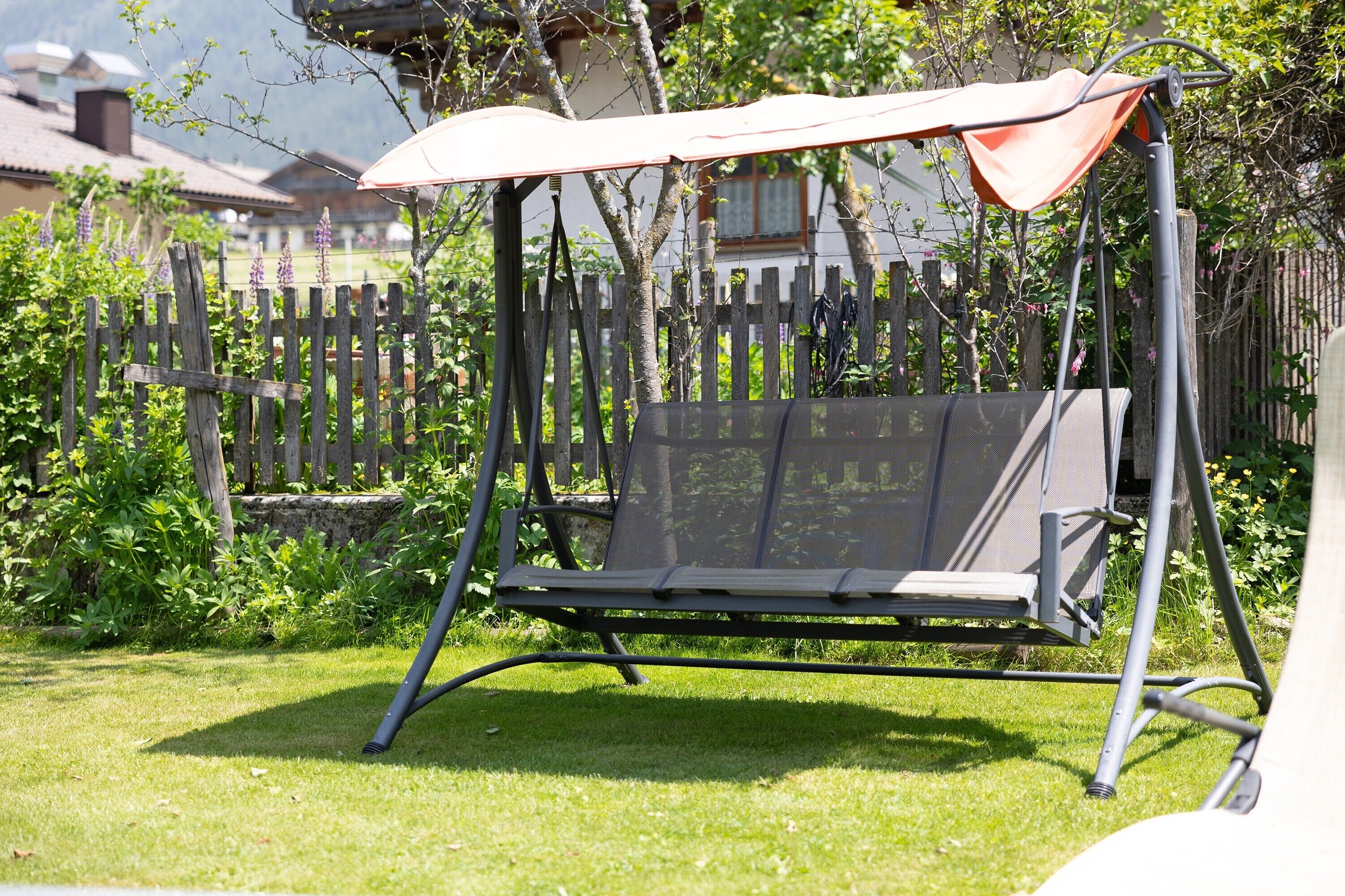 A garden with a swing set, a wooden fence, and a house in the background.