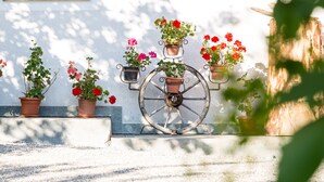 Un entorno rústico al aire libre con una maceta redonda grande y plantas en macetas, todo frente a una pared.