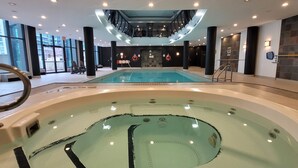 A large indoor swimming pool with a hot tub in the foreground, surrounded by black columns and a staircase leading to an upper level. - Studio for 2 in Downtown Toronto  (Toronto)